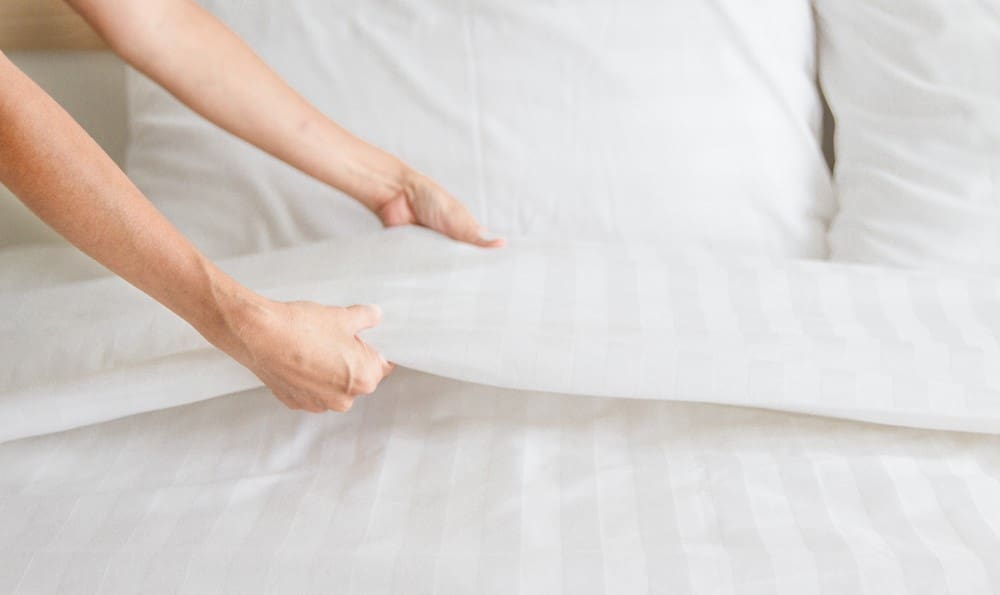 A woman is putting a white sheet on a bed.