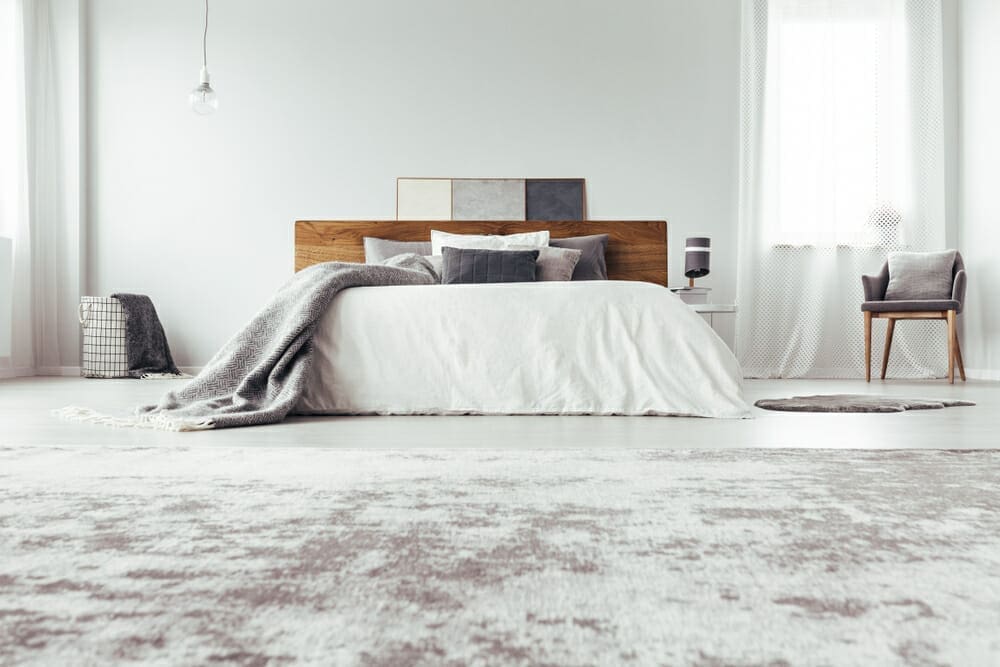 A bedroom with a white bed and a grey rug.