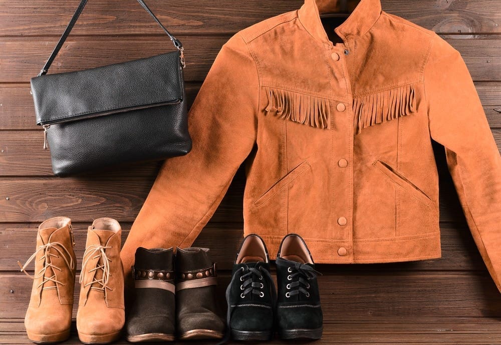 An orange jacket, boots and purse on a wooden background.