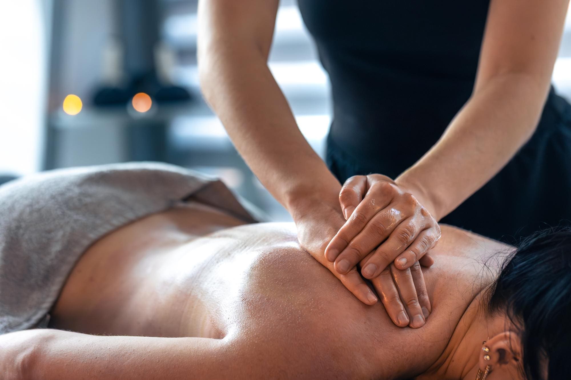 A person receives a back massage from a massage therapist in a spa setting, with a towel draped over their lower body.
