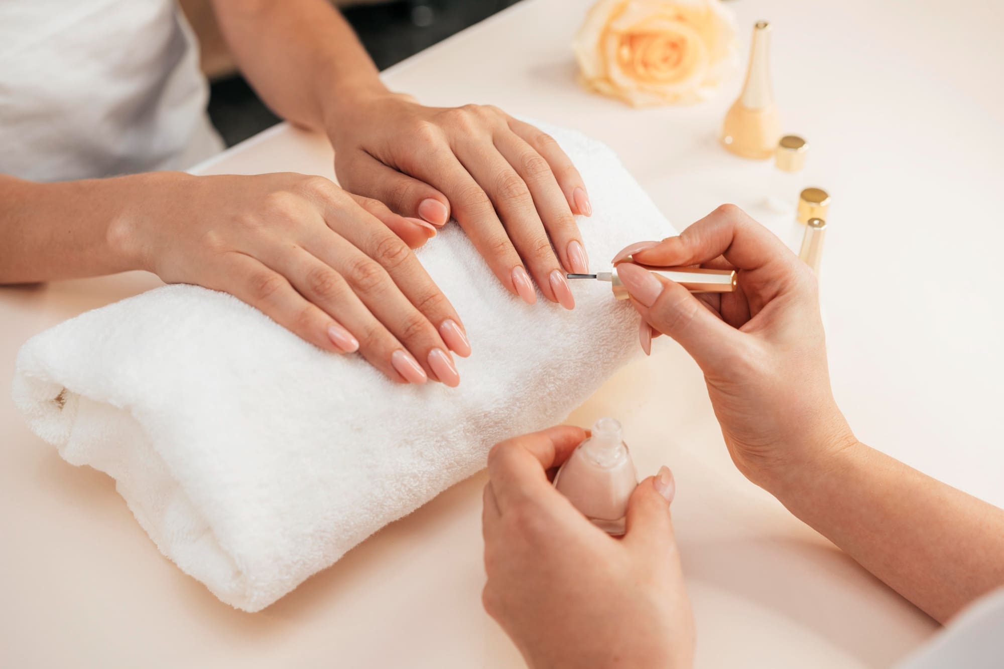A person receives a manicure, with nail polish being applied to fingernails resting on a white towel.